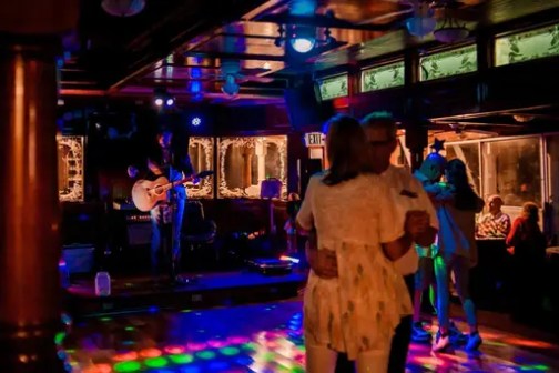 Couples dancing in a dimly lit room with a musician on stage.