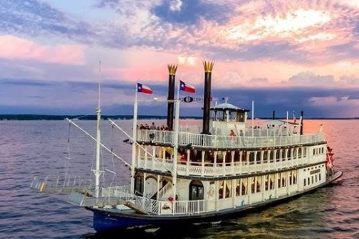 Paddle steamboat on the water at sunset with cloudy sky.