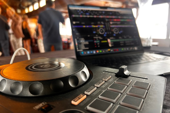 Close-up of a DJ controller and laptop with a blurred crowd in the background.