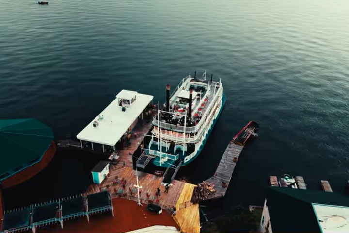Aerial view of a docked ferry on calm water with a building nearby.
