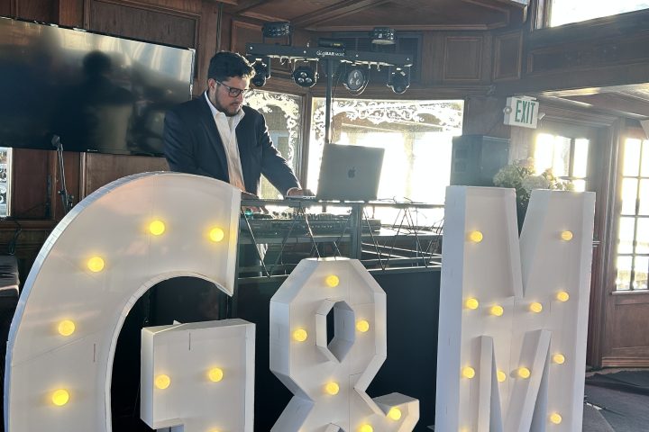 Large illuminated 'V & S' letters beside a man in a suit indoors.