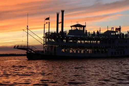 Paddle steamboat sailing during sunset on a calm river.